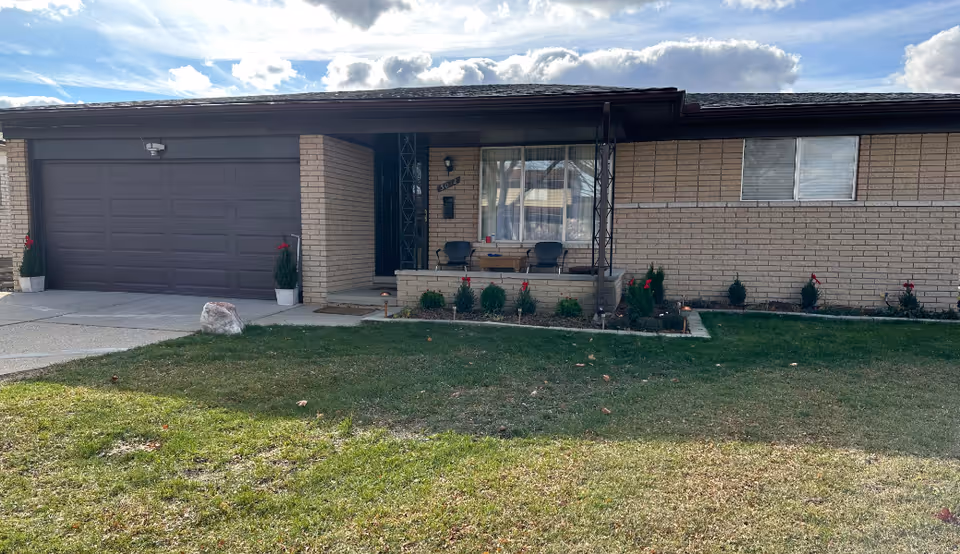 Front view of a single-story brick group home with porch seating and lawn.
