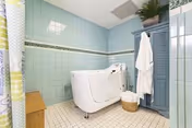 A laundry room with a top-loading washing machine, mint tiled walls, and a blue cabinet.