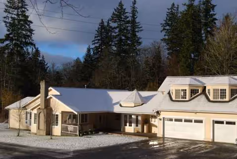 Single-story senior care facility exterior with a driveway, garage doors, and snow on the roof.