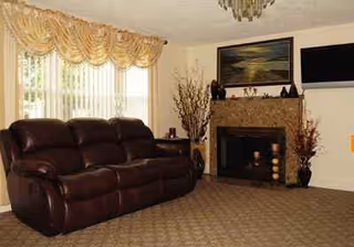 Cozy living room with brown leather sofa, fireplace, art, and window drapes.