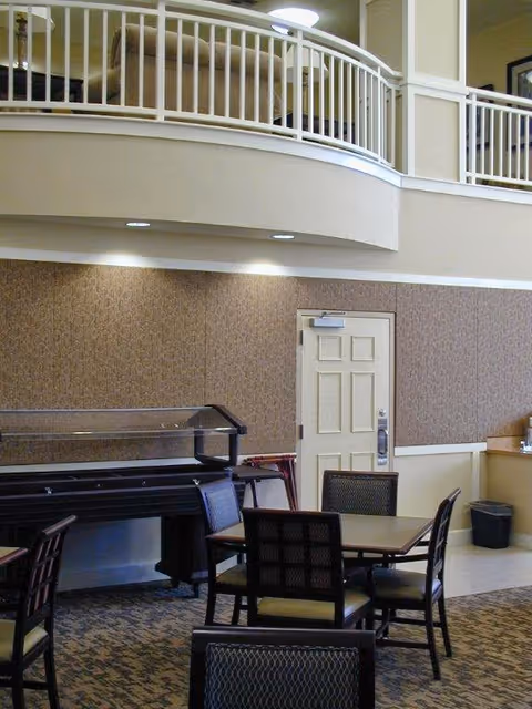 Community dining area with tables and chairs, a serving buffet, and an upper-level balcony railing.