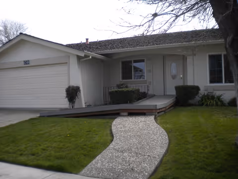 Front view of a single-story residential care home with a curved pebble walkway.