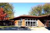 Exterior view of a single-story brick building with large windows and a flat roof, surrounded by trees with autumn foliage under a clear blue sky.