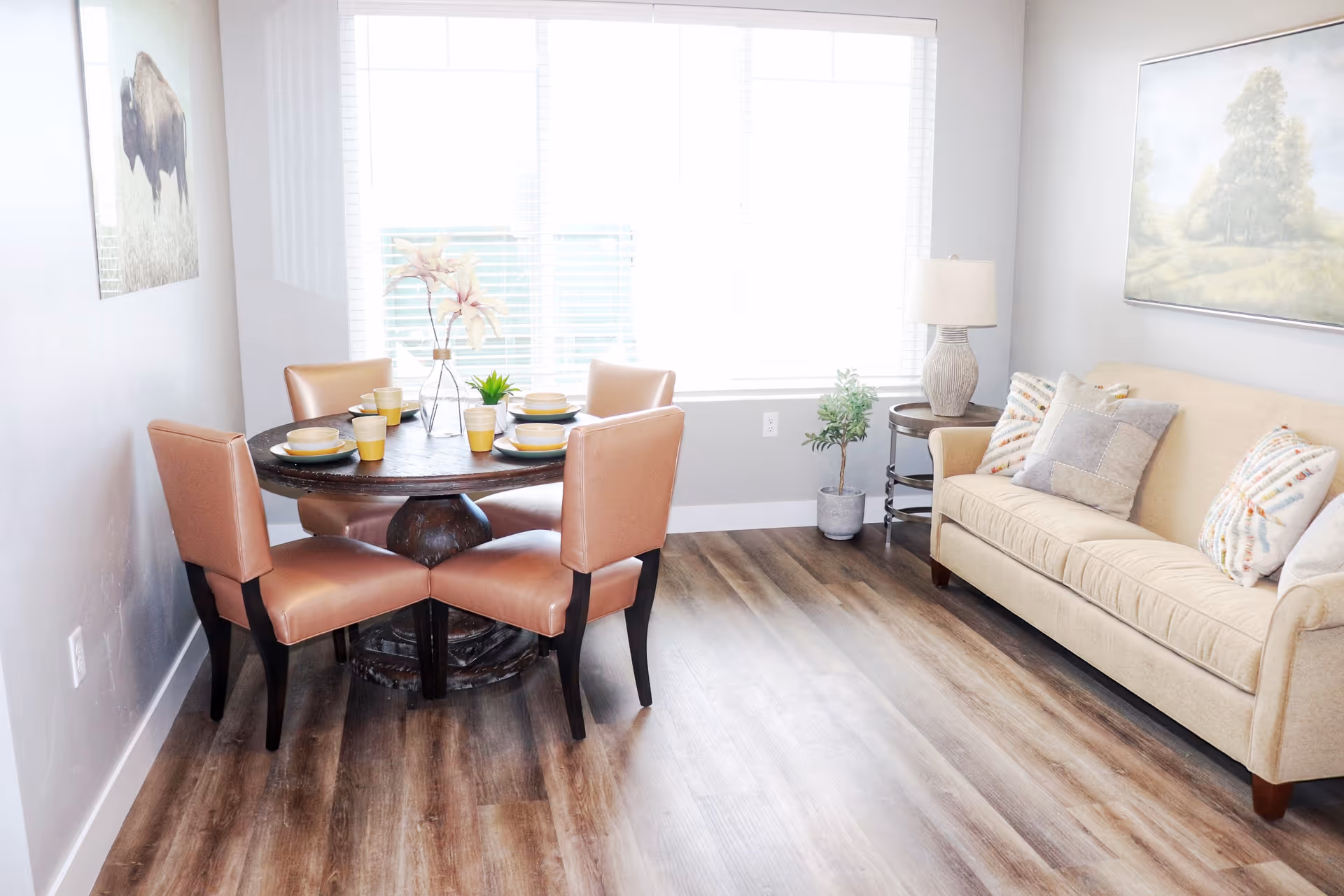 Bright living room and dining nook with a round table and four chairs, a beige sofa, and a large window.