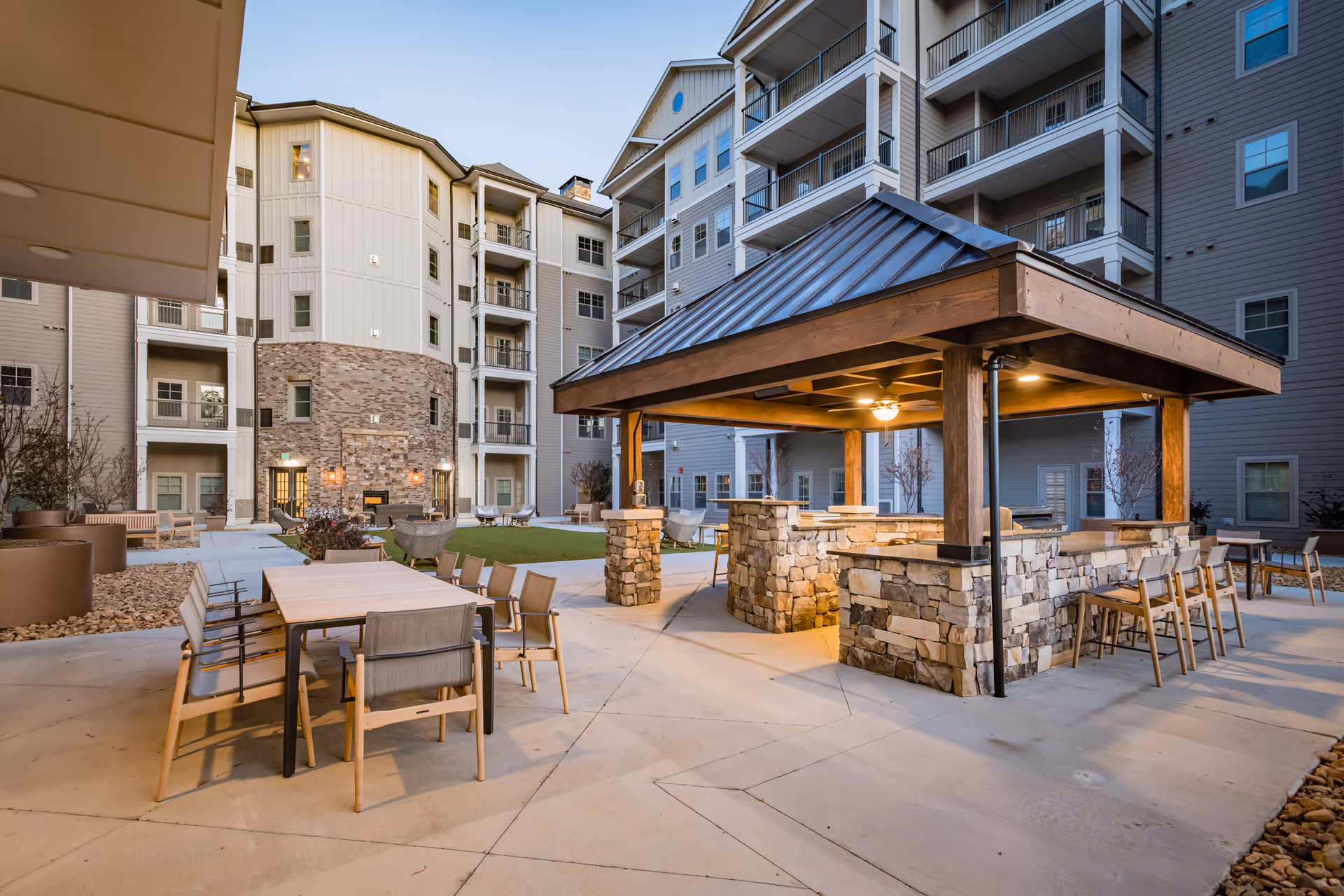 Courtyard of a senior living complex with a covered stone pavilion, outdoor dining tables, and surrounding multi-story apartment buildings.