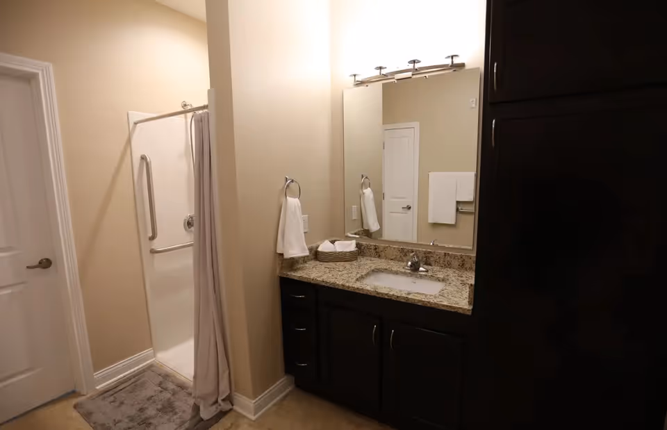 Bathroom featuring a granite-topped sink vanity with dark cabinets and a walk-in shower with a curtain.