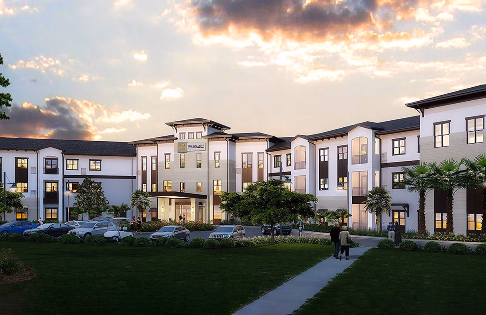 Exterior view of The Gallery at Port Orange senior living facility during sunset, showing a large, modern three-story building with multiple windows, landscaped greenery, palm trees, parked cars, and a few people walking on a sidewalk leading to the entrance.