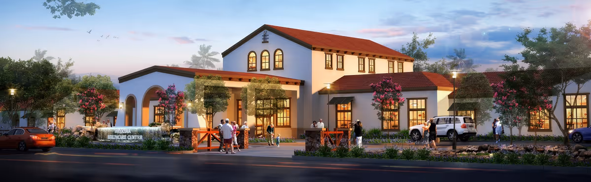 Exterior view of Temecula Memory Care facility at dusk with a Mediterranean-style building featuring white walls and a red tile roof. Several people are walking and standing near the entrance, surrounded by landscaped greenery and flowering trees. Cars are parked along the street in front of the building.