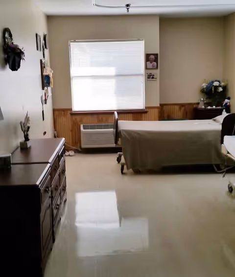 A senior living bedroom with a bed, dresser, window blinds, and wall decor.