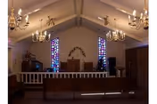 A chapel-like room in a nursing home with pews, chandeliers, and stained glass windows.
