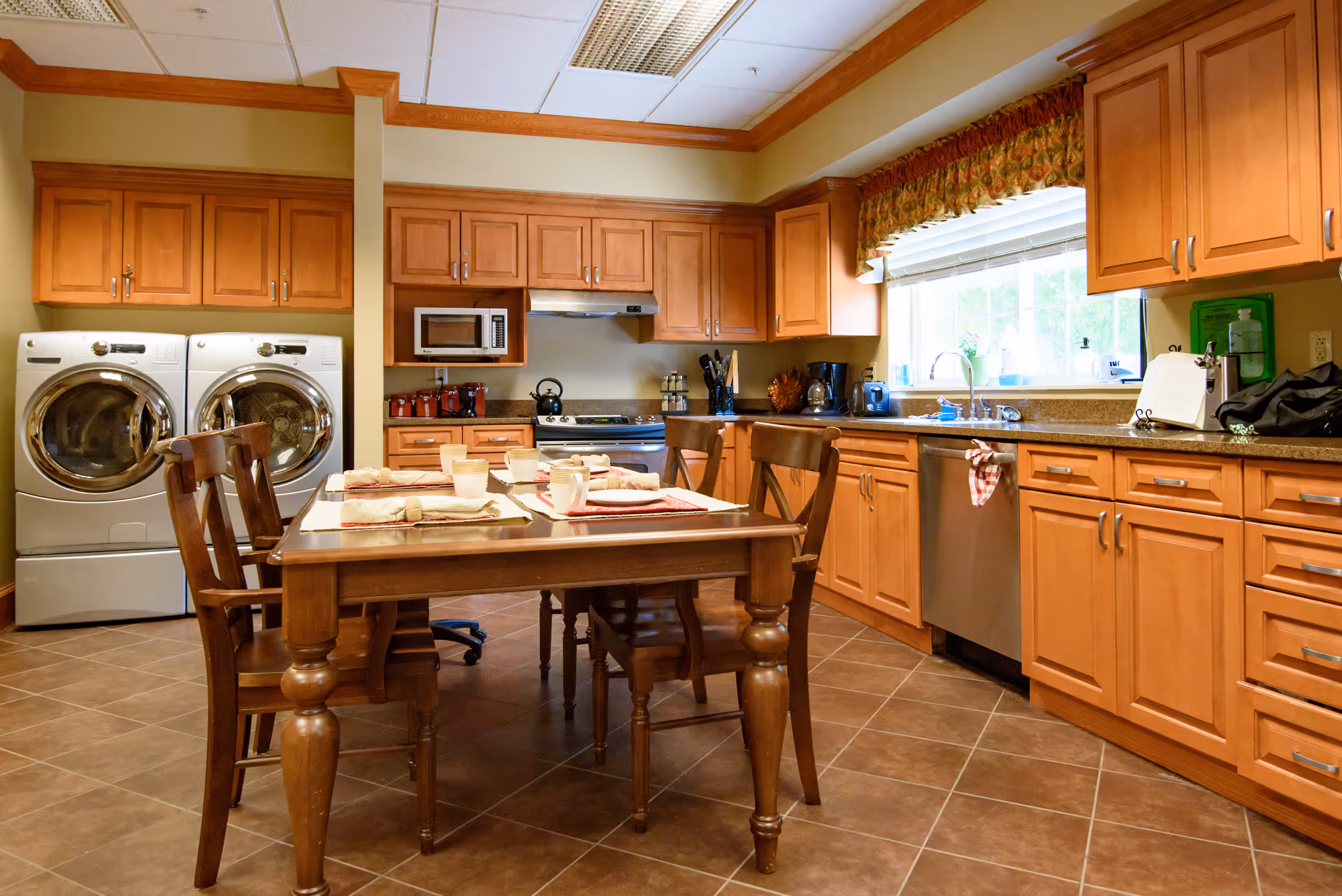 Spacious kitchen and dining area with wooden cabinetry, a table set for four, stainless appliances, and a pair of washing machines.