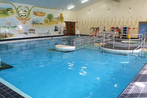 Indoor swimming pool with accessibility ramps and a mural on the far wall.