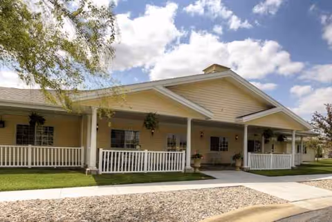 A single-story beige senior living building with a wide covered porch and white railing.