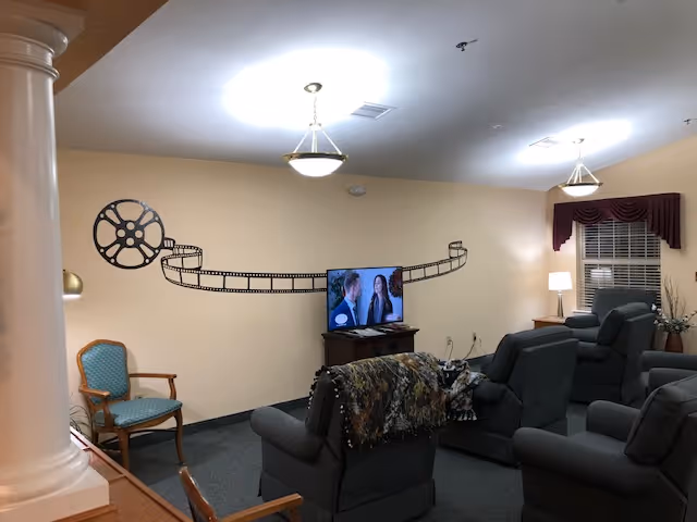 Cozy common TV room with multiple reclining chairs facing a small television and a decorative film-strip mural on the wall.