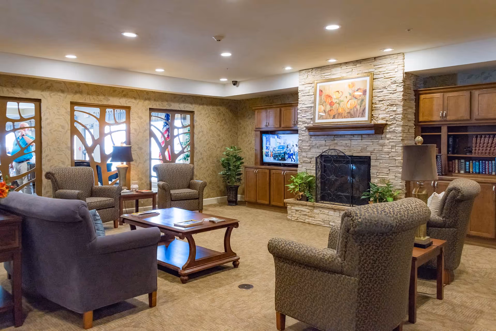 Cozy senior living lounge with armchairs and a coffee table facing a stone fireplace and built-in cabinets.