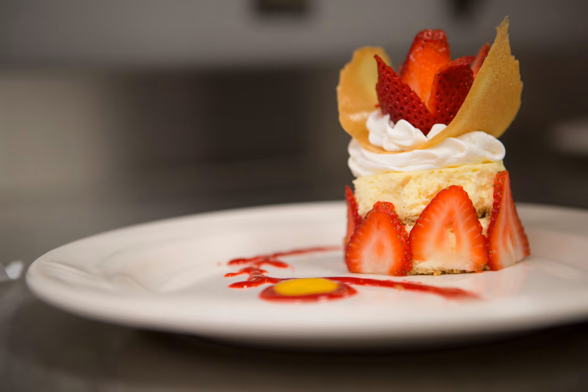 A plated strawberry-topped dessert with whipped cream and sauce on a white plate.