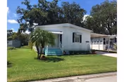 Single-story mobile home with a small porch, green lawn, and palm trees in front.