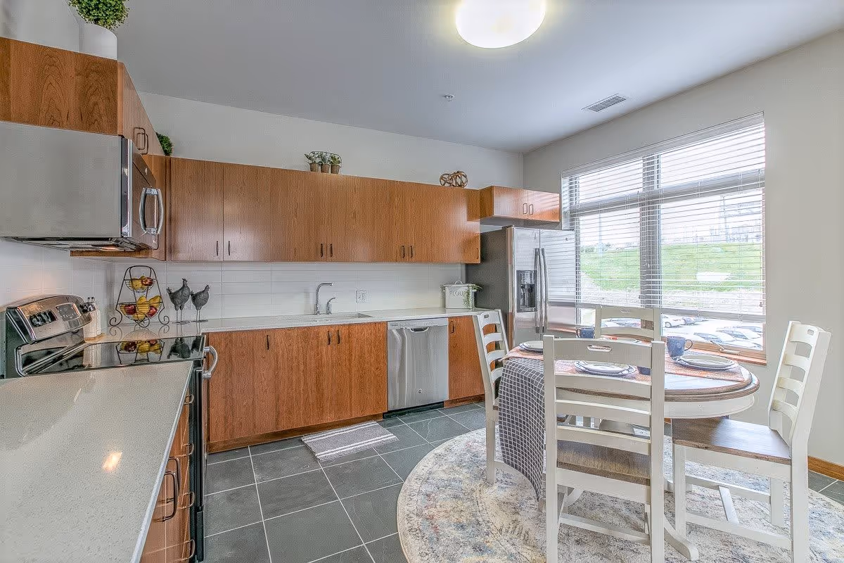 Modern kitchen with wood cabinets, stainless-steel appliances and a round dining table by a large window.
