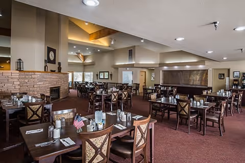 Spacious dining room with multiple set tables and chairs, a stone fireplace, and warm overhead lighting.