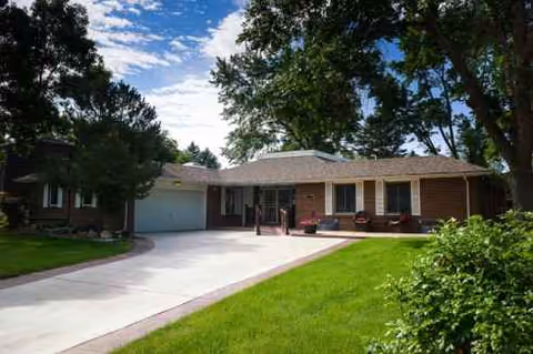 Single-story brick building with a driveway, front porch seating, and a green lawn.