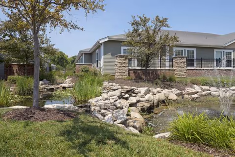Exterior view of a StoneBridge Senior Living building with landscaped rocks, pond, and trees.