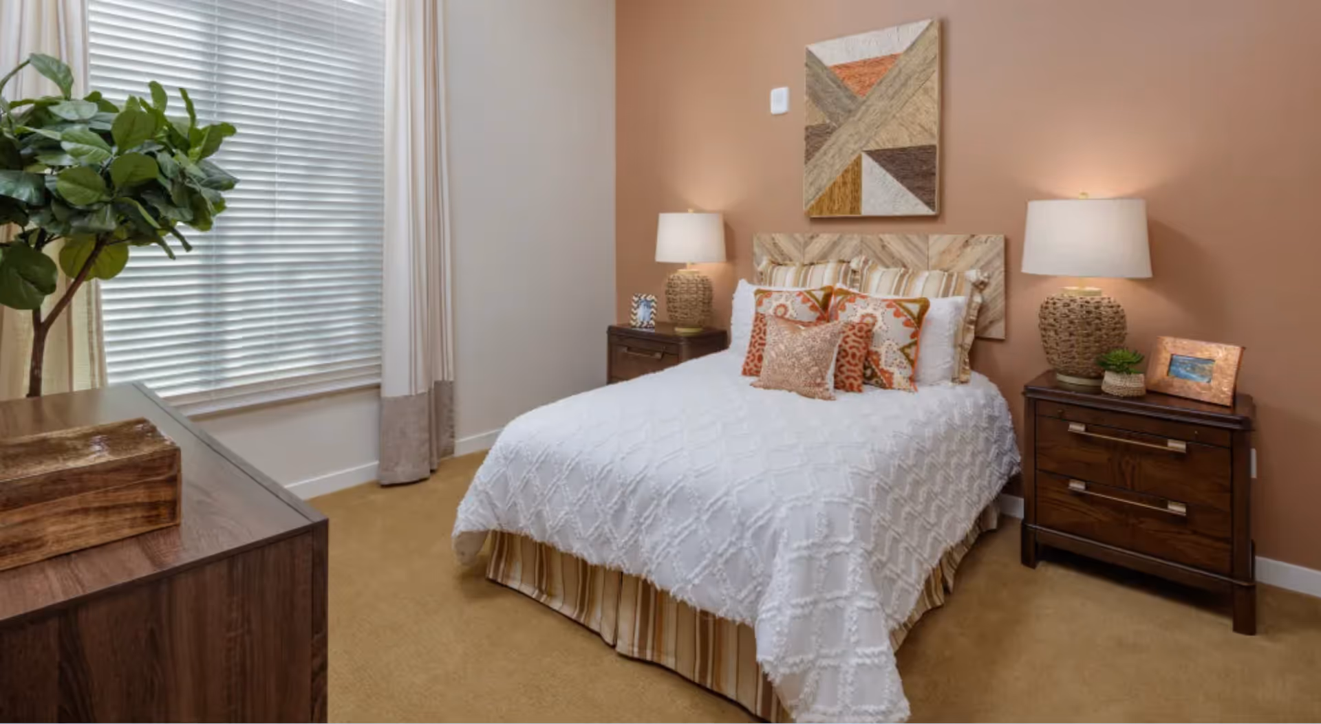 Well-lit furnished bedroom with a double bed, two bedside tables and lamps, a window with blinds, and decorative accents.