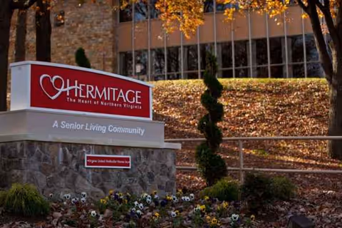 Exterior view of Hermitage senior living sign with stone base and autumn landscaping.