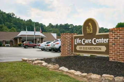 Exterior view of Life Care Center of Elizabethton with brick sign and parked cars.