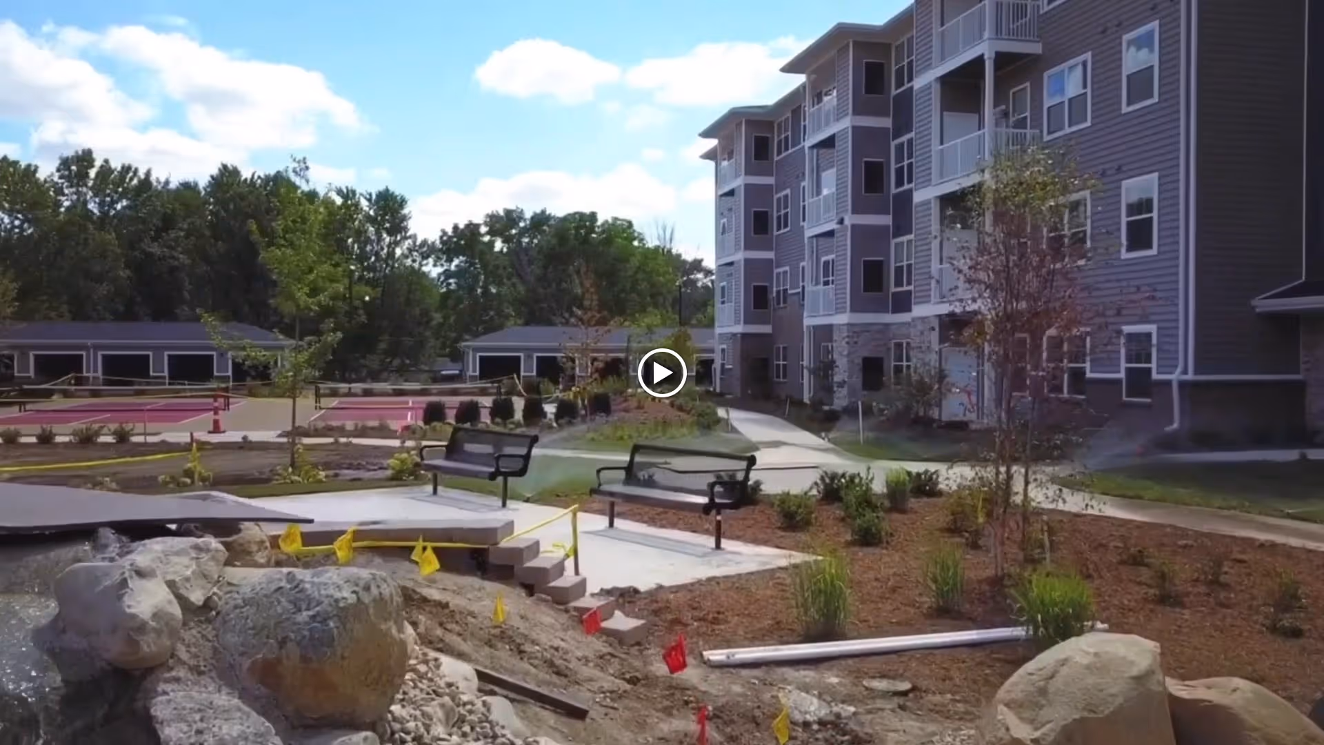 Courtyard with benches, landscaping and a water feature in front of a multi-story apartment building under a blue sky.