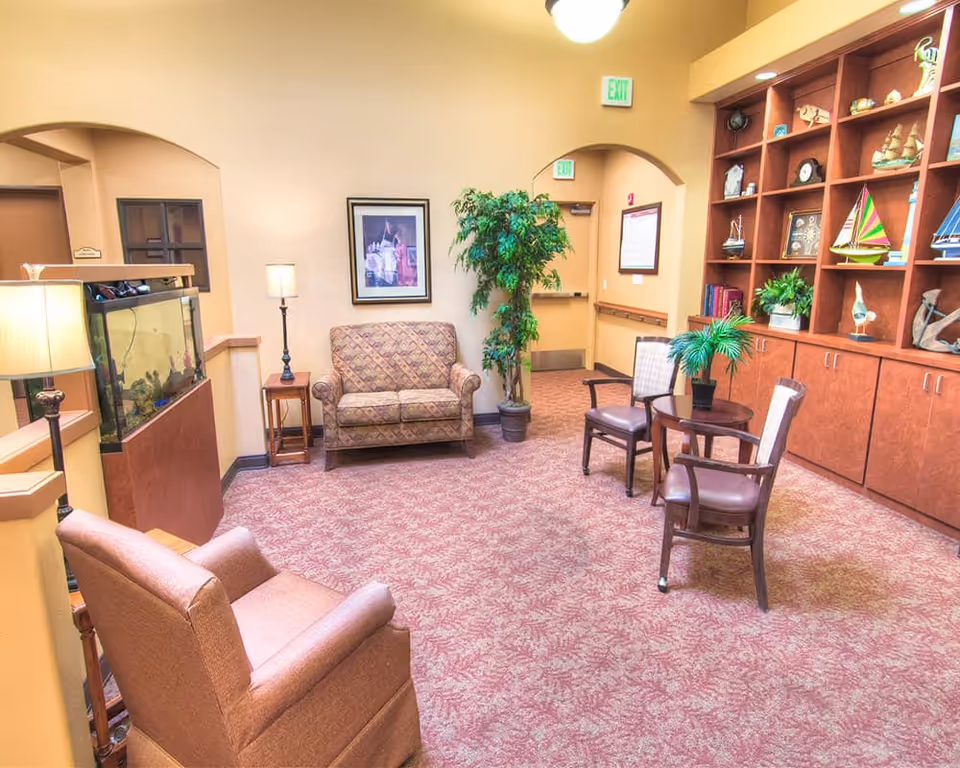 Well-lit seating area with upholstered chairs and a loveseat, small table and chairs, built-in shelving with decor, a potted plant and a fish tank.
