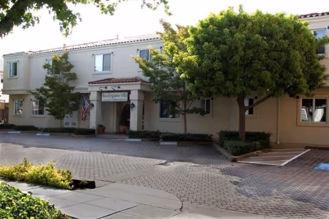 Exterior view of Burlingame Villa senior living facility entrance with trees and a parking lot.