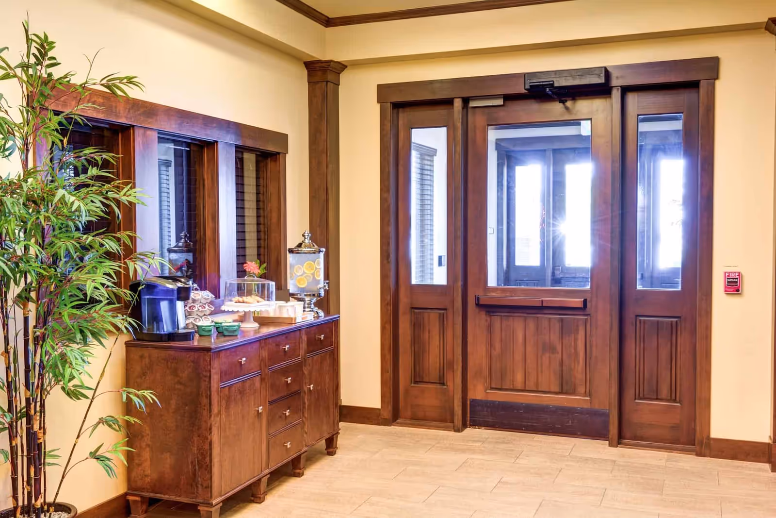 Interior entry area with wooden double doors, a console table holding a coffee maker and refreshments, and a tall potted plant.