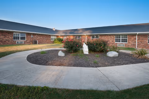 A brick senior living center with a circular driveway and landscaped center featuring rocks and flowers.