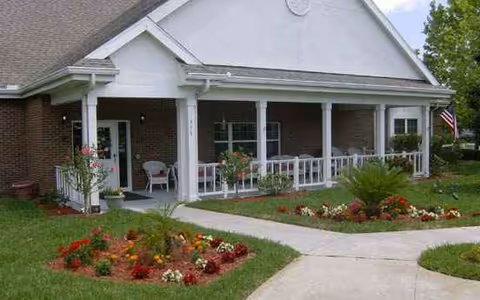 Front exterior view of a senior living facility with a covered porch and flower beds.
