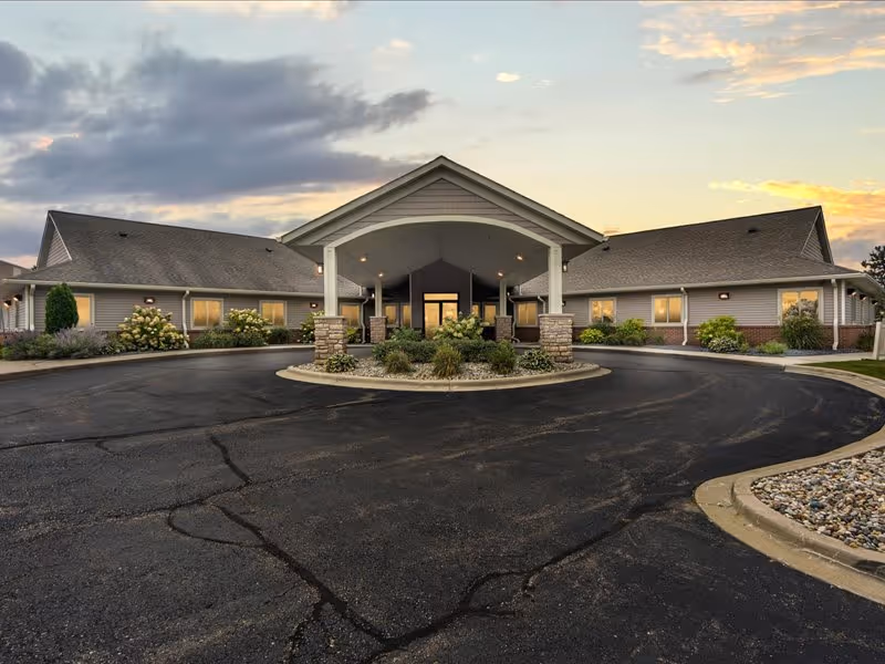 Single-story senior care building with a covered porte-cochere and circular driveway at dusk.