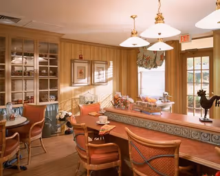 Warmly decorated dining area with a long wooden counter and upholstered bar stools, tables, pendant lights, and display cabinets.
