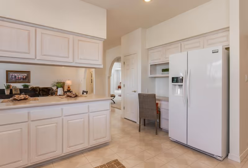 Bright kitchen with white cabinets, a large refrigerator, and a counter overlooking a living area.