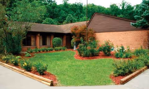 Brick senior living facility exterior with green lawn, mulch beds, and shrubs.