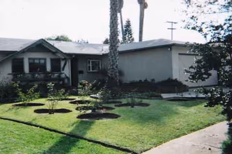 Front exterior of a single-story senior living facility with manicured lawn and shrubs.