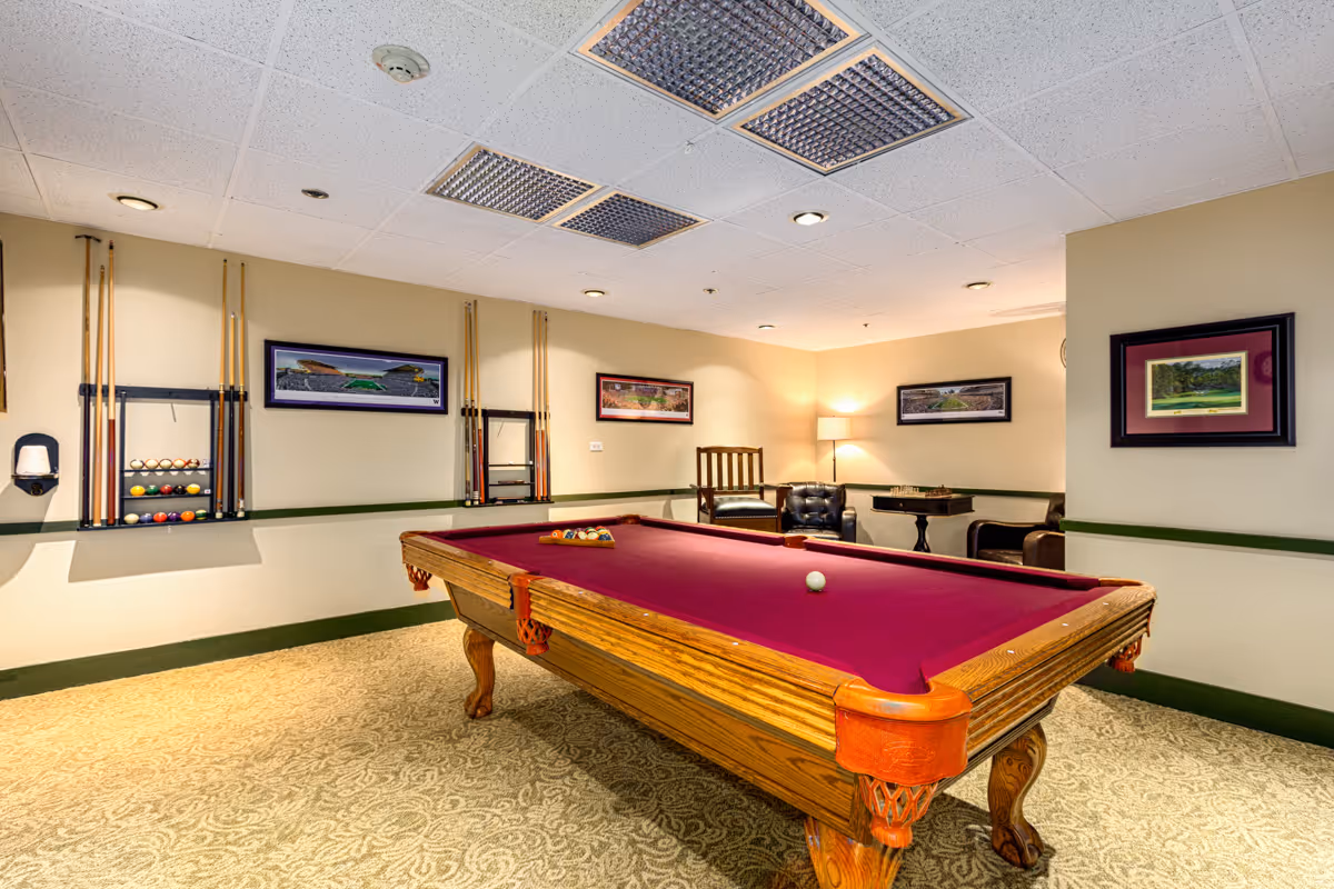 Recreation room featuring a wooden pool table with burgundy felt, cue racks, seating, and framed artwork on the walls.