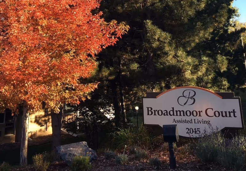 Broadmoor Court Assisted Living entrance sign among trees and fall foliage.