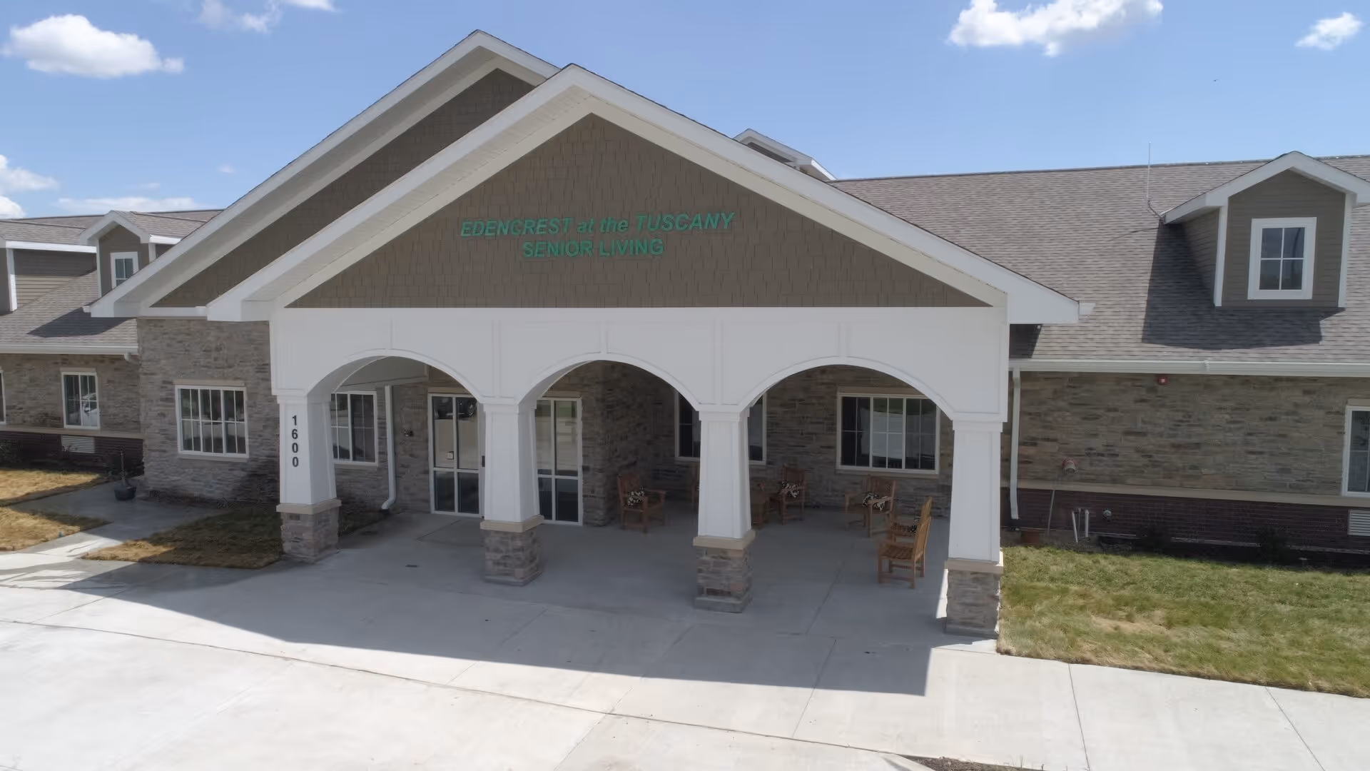 Front entrance of Edencrest at The Tuscany senior living building with a covered porte-cochere and outdoor chairs.