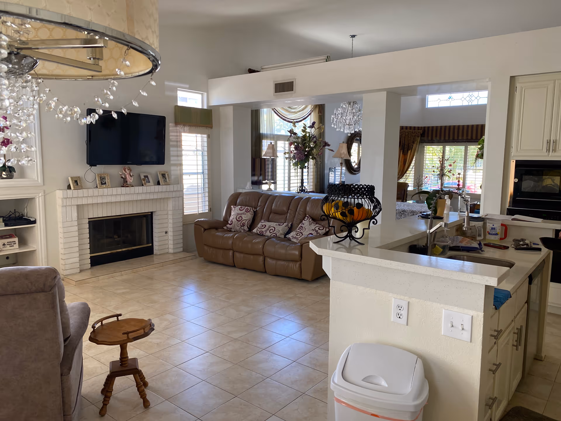 Bright open-plan living room and kitchen with tile floors, a leather sofa, fireplace with wall-mounted TV, and a countertop island.