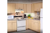 Small U-shaped kitchen with light wood cabinets, a white stove and refrigerator, microwave, sink, and countertop accessories.