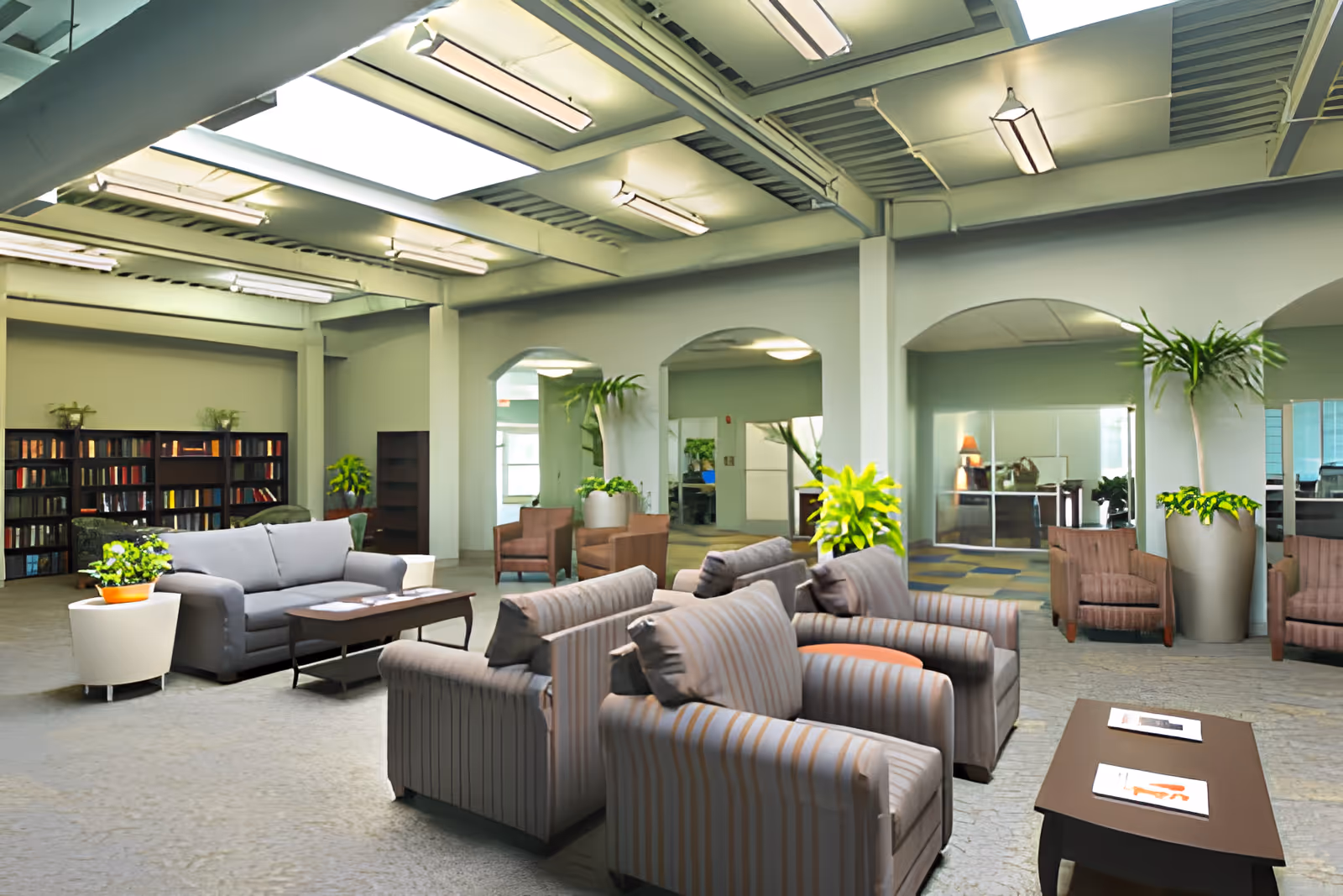 Spacious, well-lit communal lounge with sofas, armchairs, coffee tables, plants and bookshelves under skylights.