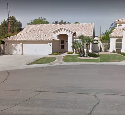 Single-story residential building with a tiled roof, a three-car garage, a small front lawn with palm trees, and a paved driveway, situated on a curved street.