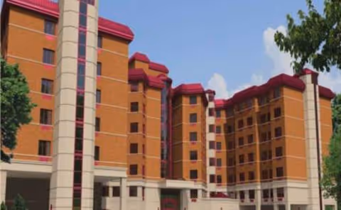 Multi-story brick senior living building with tan columns and red roof accents against blue sky.