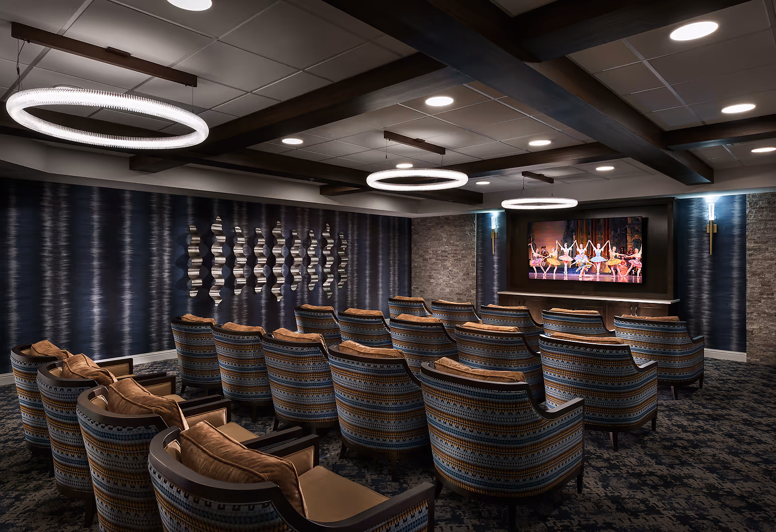 A cozy theater-style screening room with rows of patterned armchairs facing a large wall-mounted TV and modern circular ceiling lights.