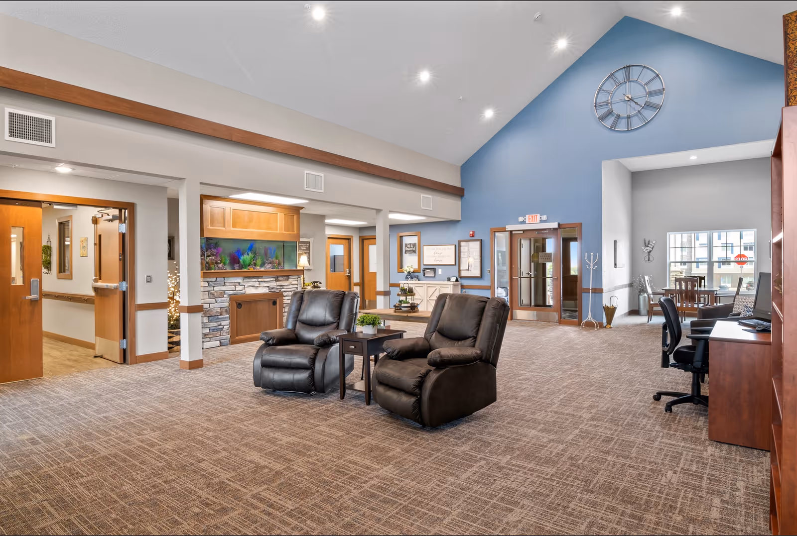 Spacious lobby-style common room with two recliners, side table, reception desk, aquarium and a vaulted blue accent wall with a large clock.