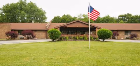 Front view of Aperion Care Tolleston Park building with flagpole and manicured lawn.